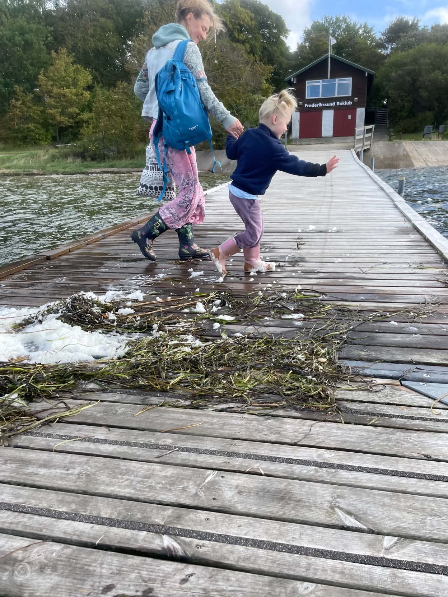 En voksen og et barn går hånd i hånd på badebroen