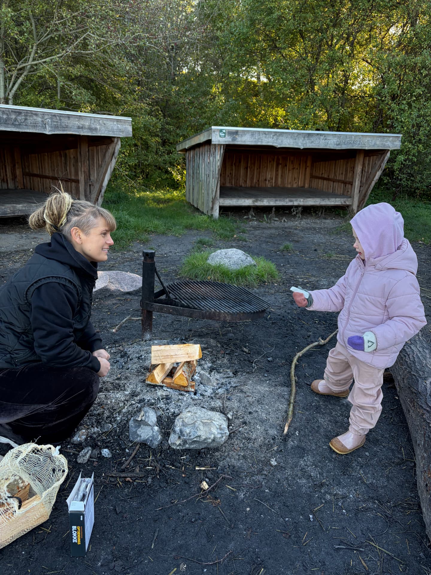 En voksen og et barn samlet om bålet mellem shelterne